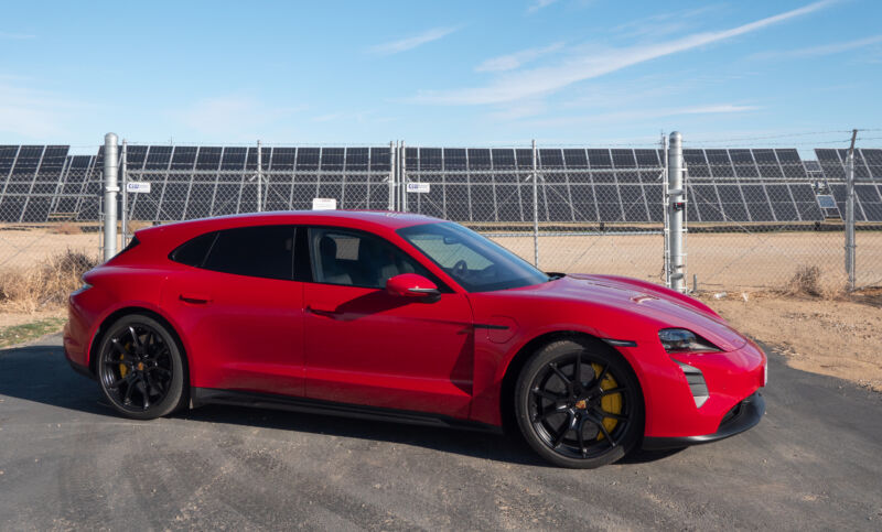 A red Porsche Taycan GTS Sport Turismo next to a solar panel farm