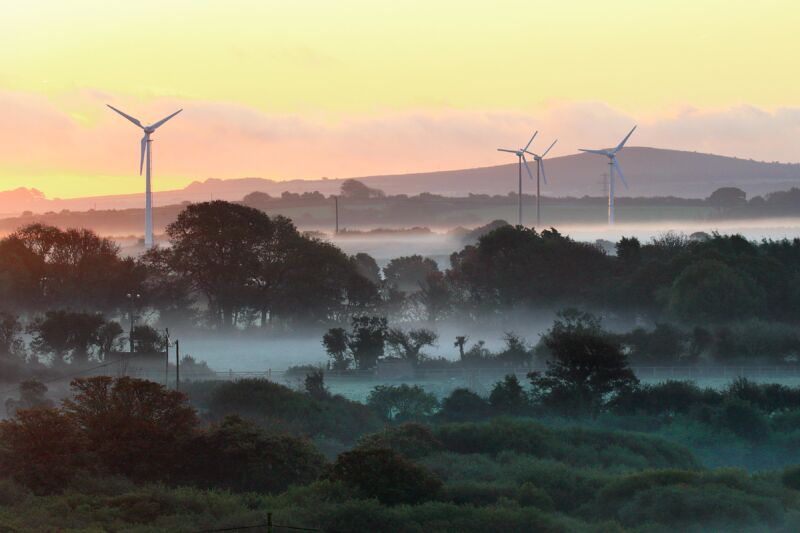 Wind turbines loom over a foggy forest.