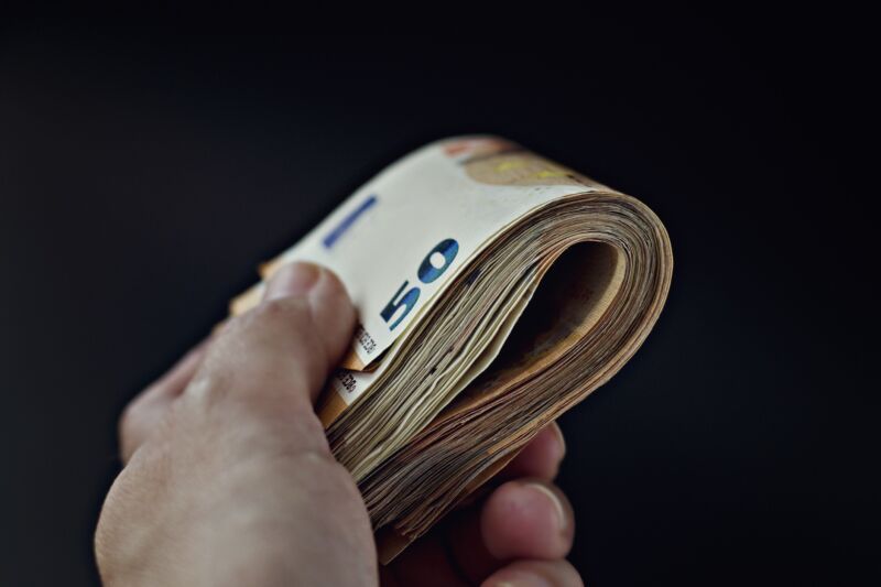 A person's hand holding a roll of 50-Euro notes.