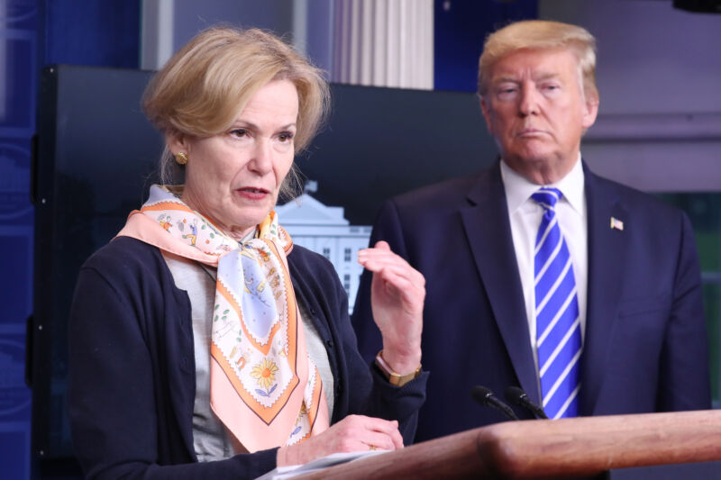 An older man in a business suit listens to a woman in a business suit.