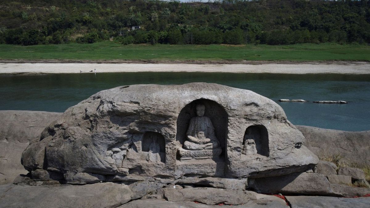 Three Buddhist statues in a dried up riverbed