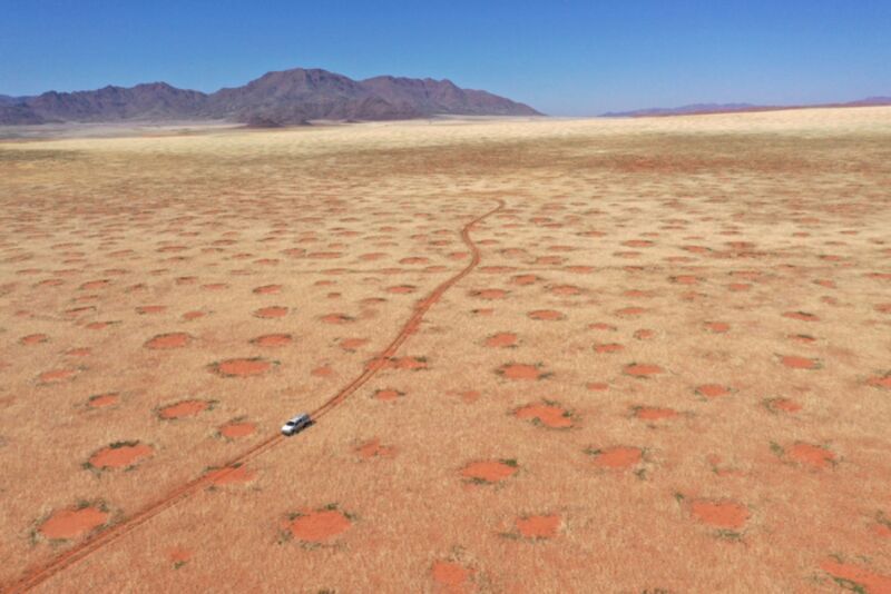 Drone image of car driving through the NamibRand Nature Reserve, one of the fairy-circle regions in Namibia.