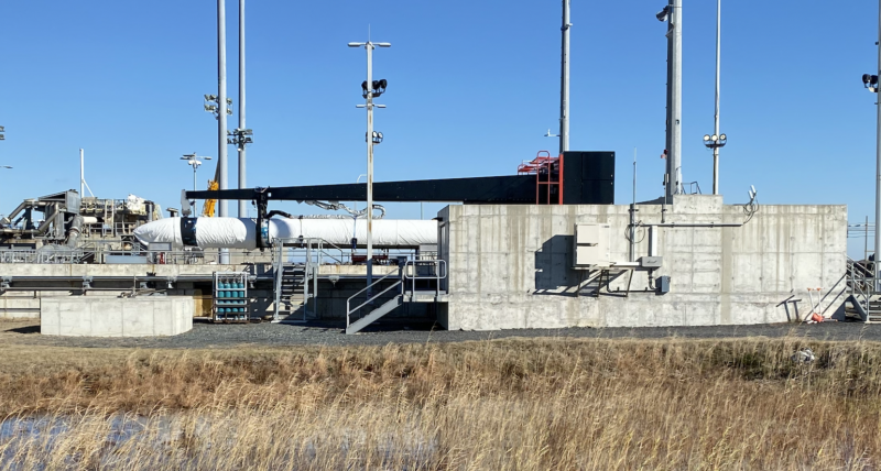 Image of a white rocket tilted horizontally and partially obscured by a concrete barrier.