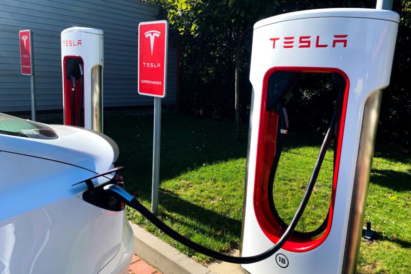 A Tesla car connected with a cable to a supercharger.