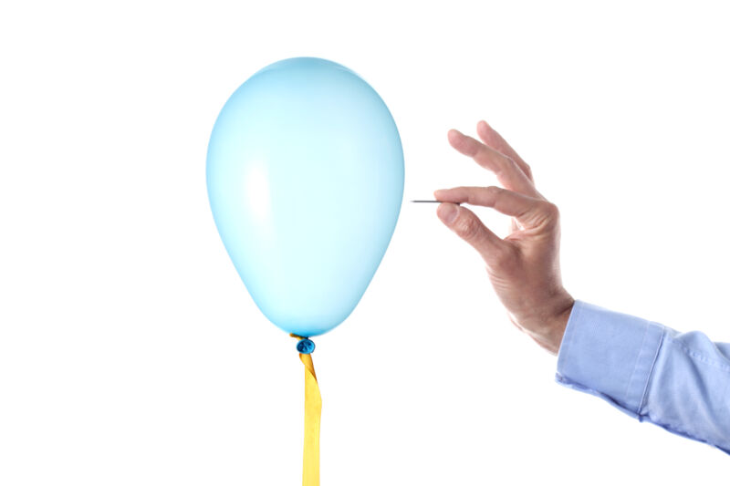 Image of a hand holding a needle to a balloon.