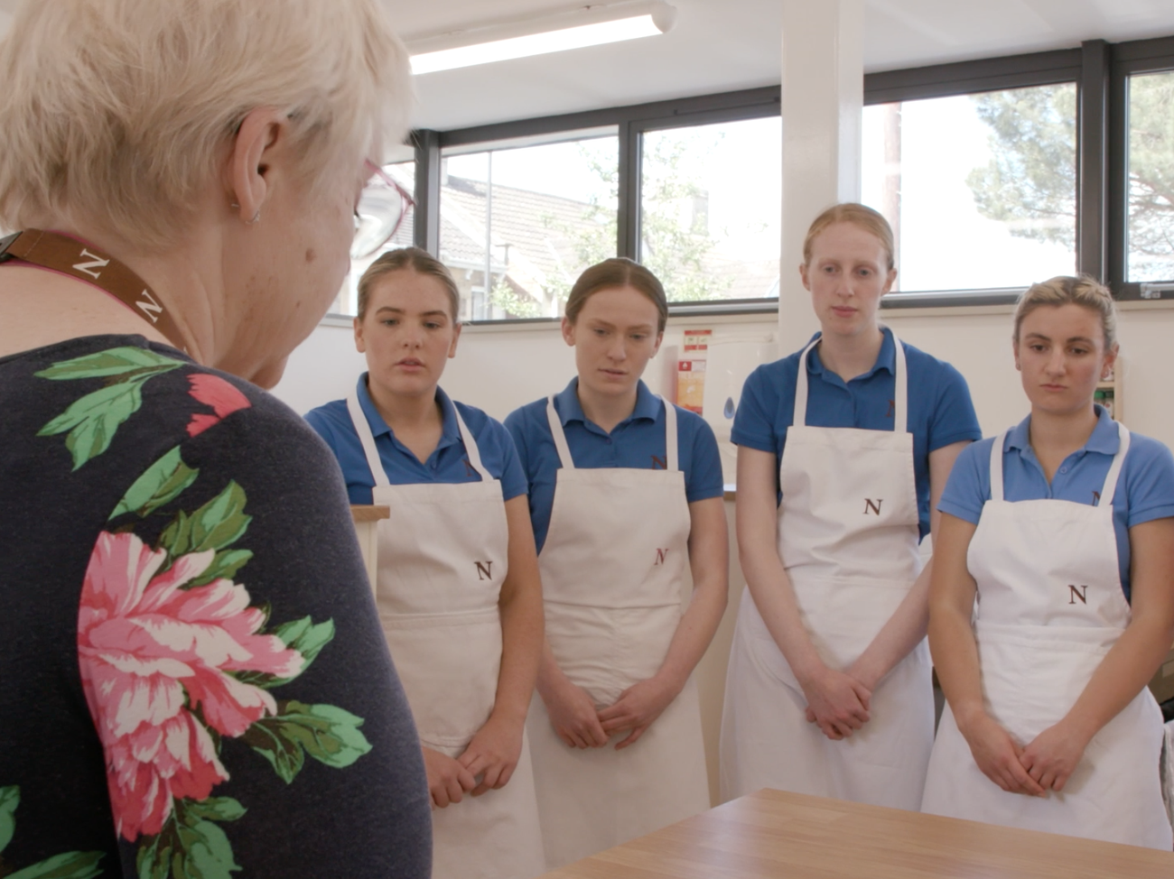 5 students in aprons listen to a cooking teacher