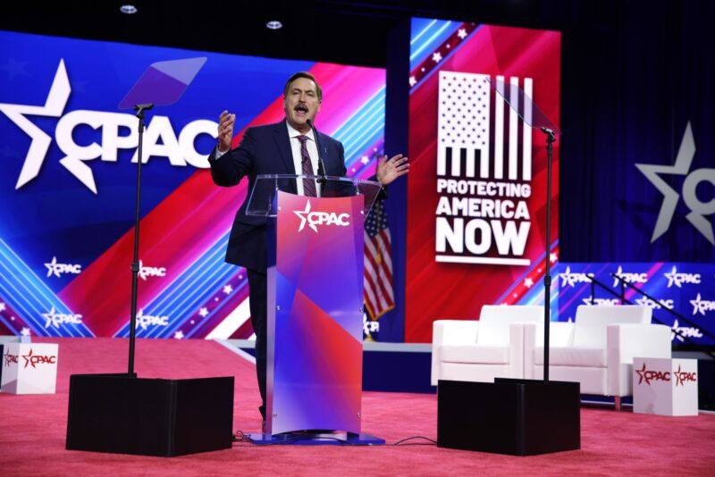 Mike Lindell speaks on stage at the Conservative Political Action Conference, flanked by signs that say 