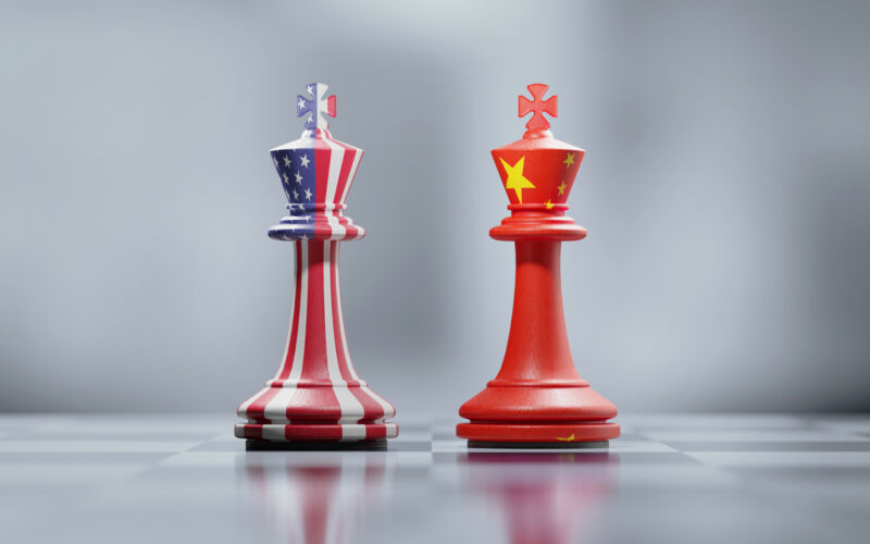 Two king chess pieces textured with American and Chinese flags on black and white chessboard.