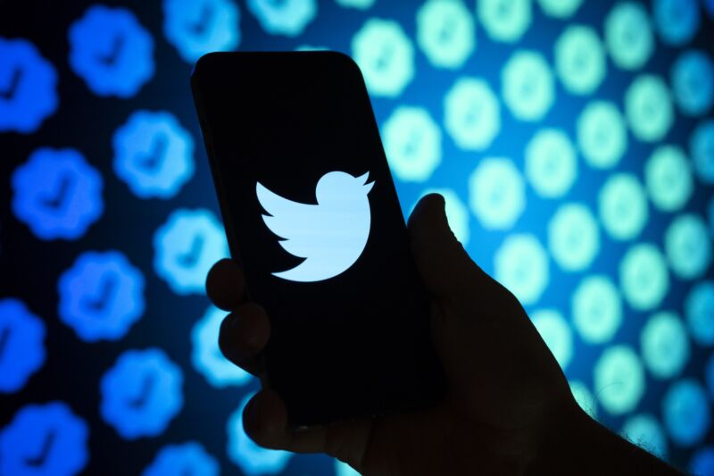 Photo illustration shows the Twitter logo on a phone screen with checkmarks in the background behind the phone.