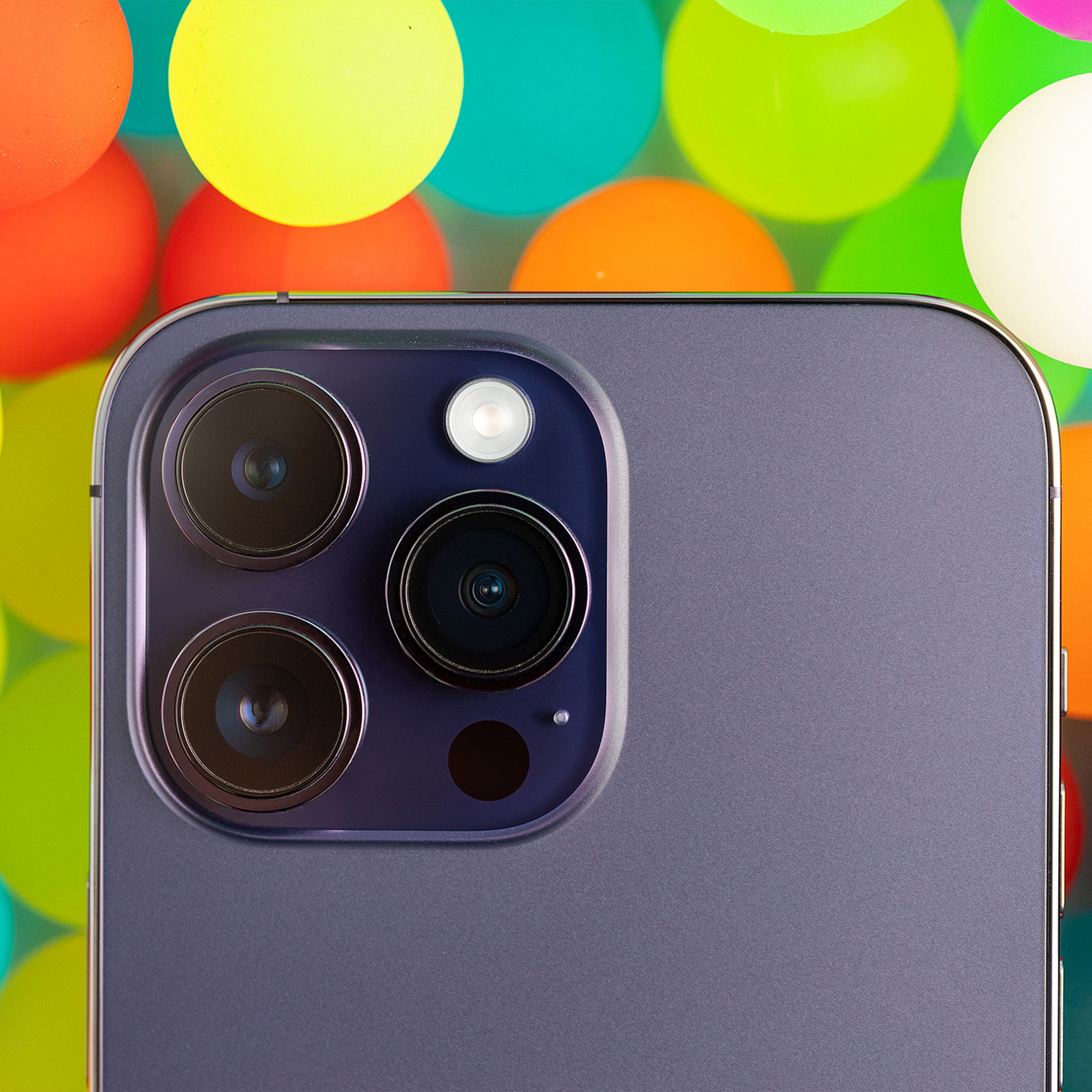 A close up image of the iPhone 14 Pro’s camera module on a background of translucent colorful balls.