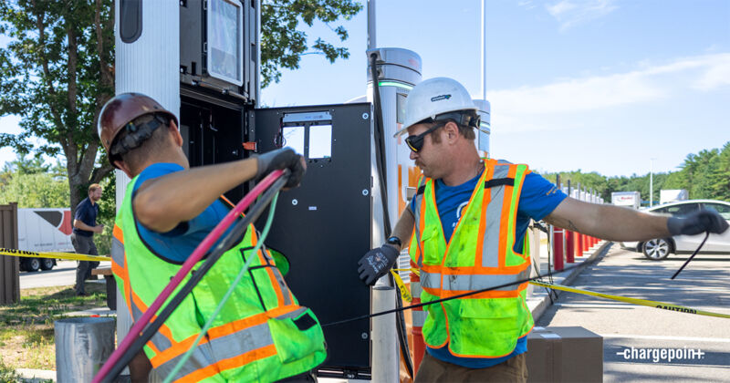 Two men in hi-viz and hardhats work on an EV charger