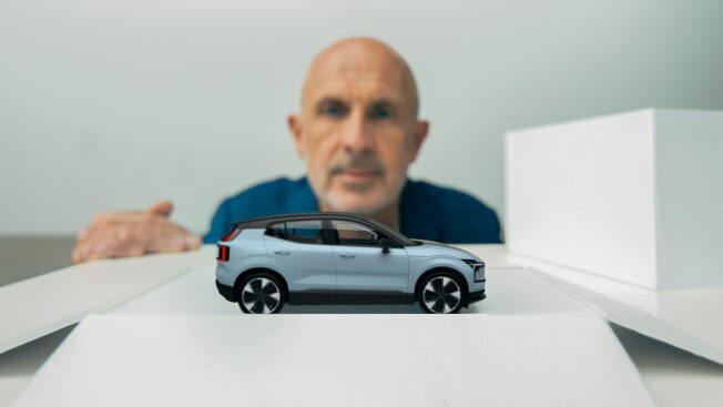 A man looking at a miniature car in an opened white box in the foreground.