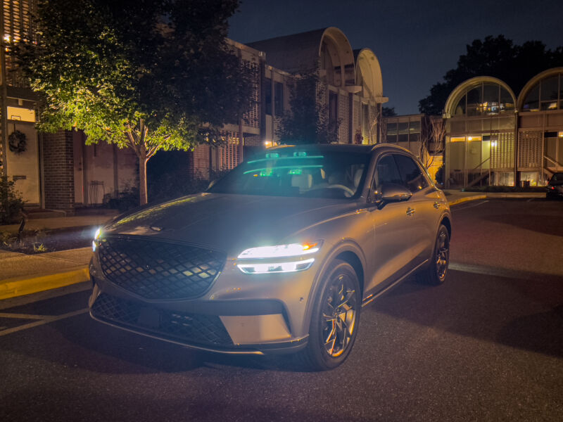 A Genesis Electrified GV70 at night, in front of mid-century townhouses