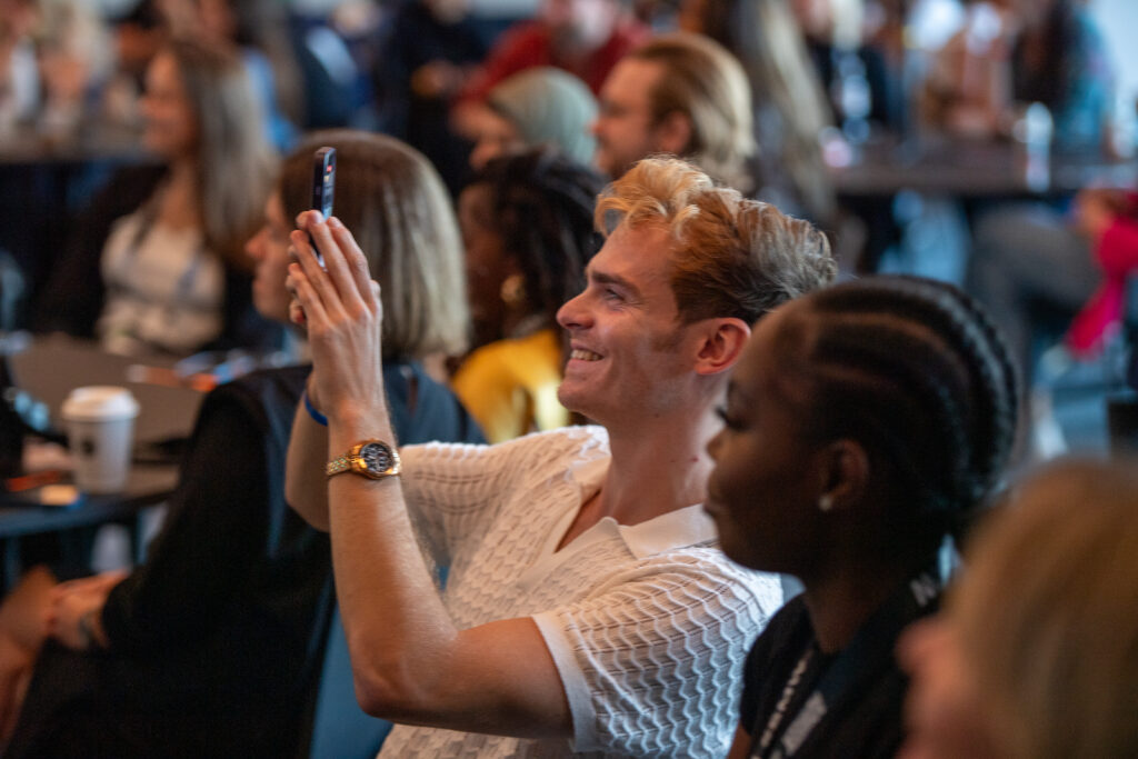 a blond man taking a cellphone photo in a crowd of people