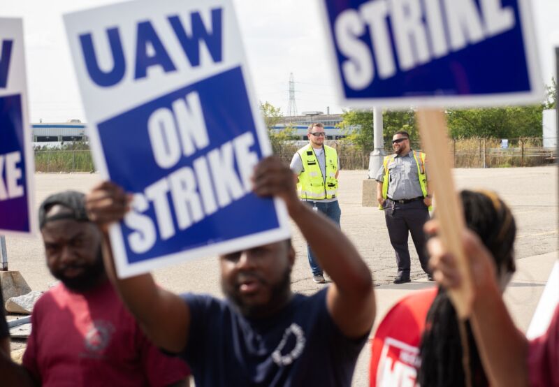 people hold strike signs saying UAW ON STRIKE