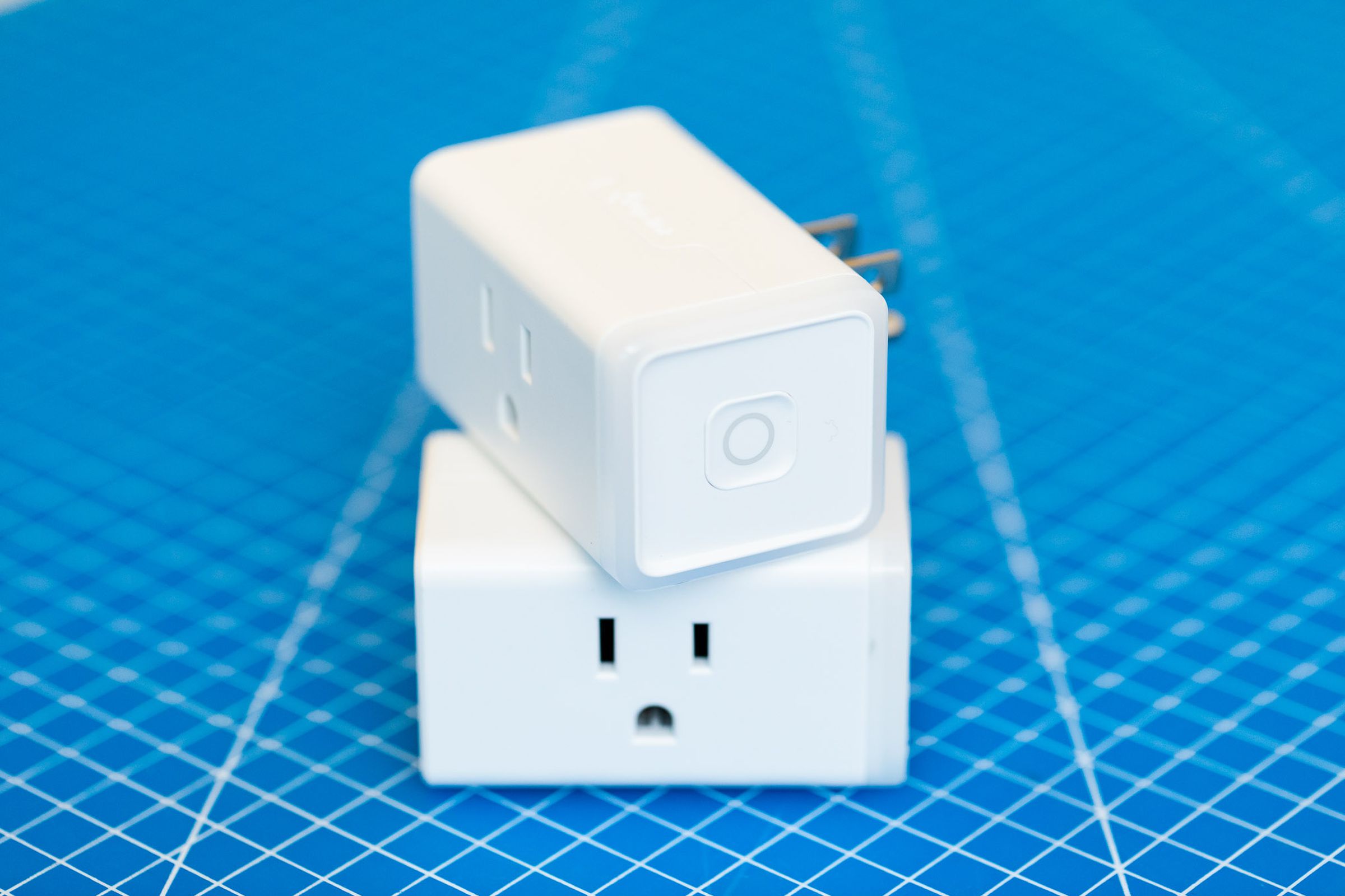 Two TP-Link Kasa KP125M Matter smart plugs stacked on top of each other. They are white rectangular prisms with a three-prong outlet on the front face and three-prong plug on the rear face, TP-Link on the top face, and a power button on the right face. 