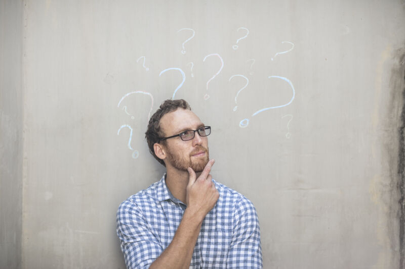 Image of a person staring pensively, with question marks drawn on the wall behind him.