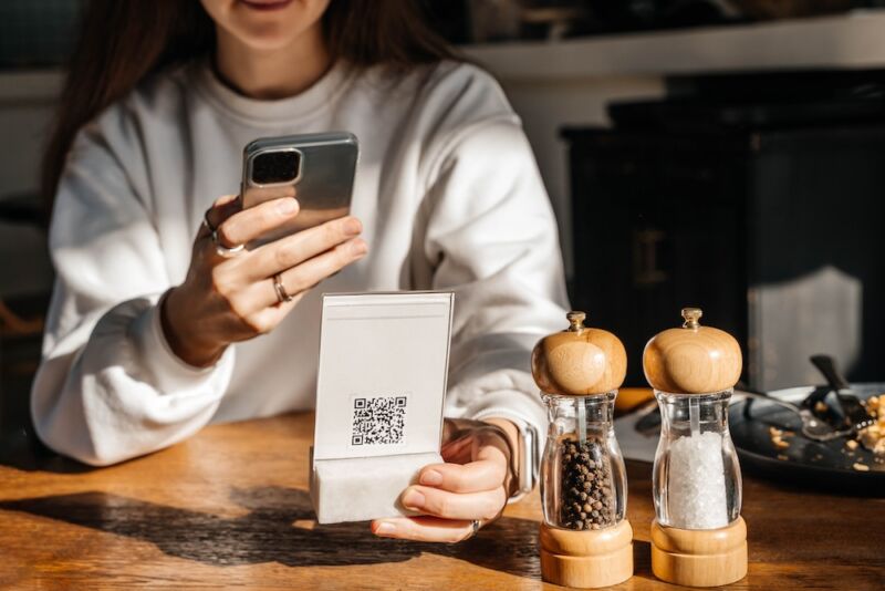 A woman scans a QR code in a café to see the menu online.