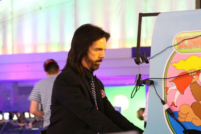 A long-haired man plays a late '70s / early '80s video game cabinet.