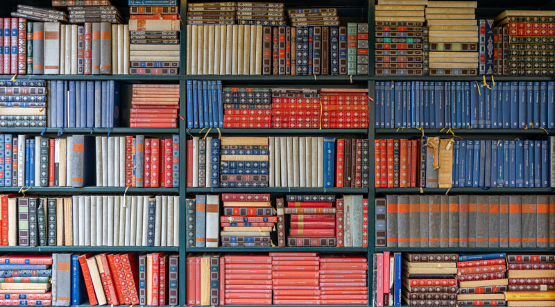 A set of library shelves with lots of volumes stacked on them.