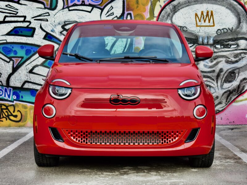 A head-on shot of a red Fiat 500e in front of a mural