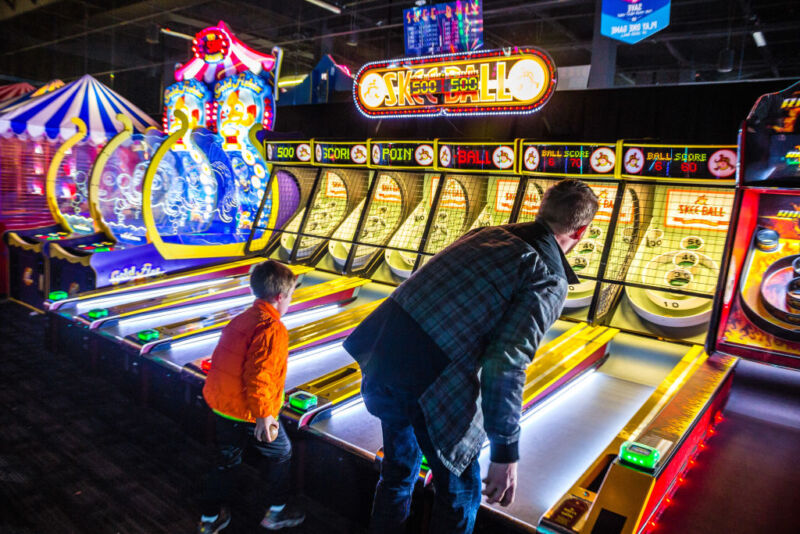 It's a good thing this kid is too young to bet on Skee-Ball, because his dad is getting <em>beat</em>.”><figcaption class=