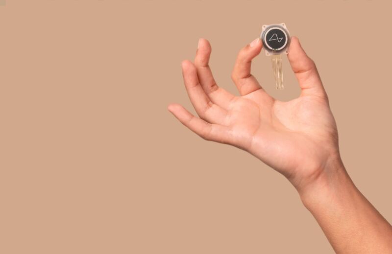 A person's hand holidng a brain implant device that is about the size of a coin.