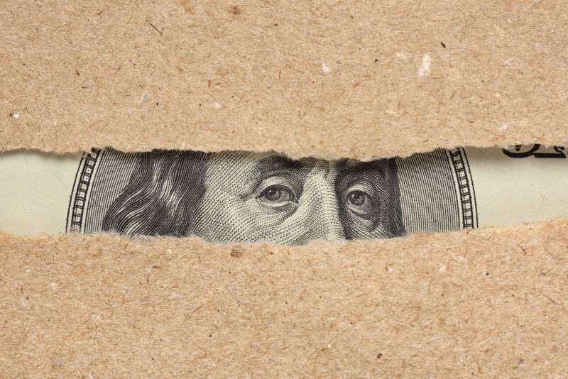 One hundred dollar bill Benjamin Franklin portrait looks behind brown craft ripped paper