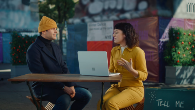 a couple sitting at a picnic table with an open laptop