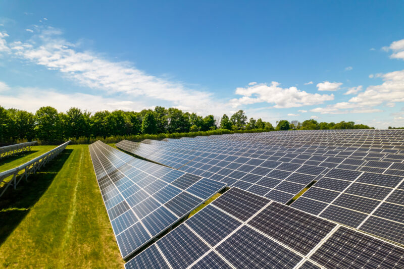 Image of solar panels on a green grassy field, with blue sky in the background.