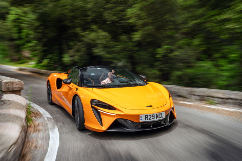 An orange McLaren Artura Spider drives on a twisy road