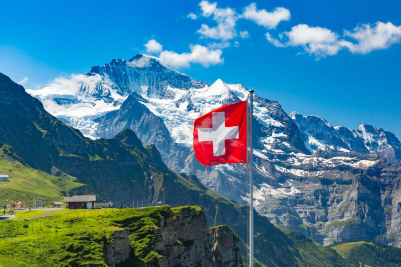 Swiss flat flying over a landscape of Swiss mountains, with tourists looking on from nearby ledge