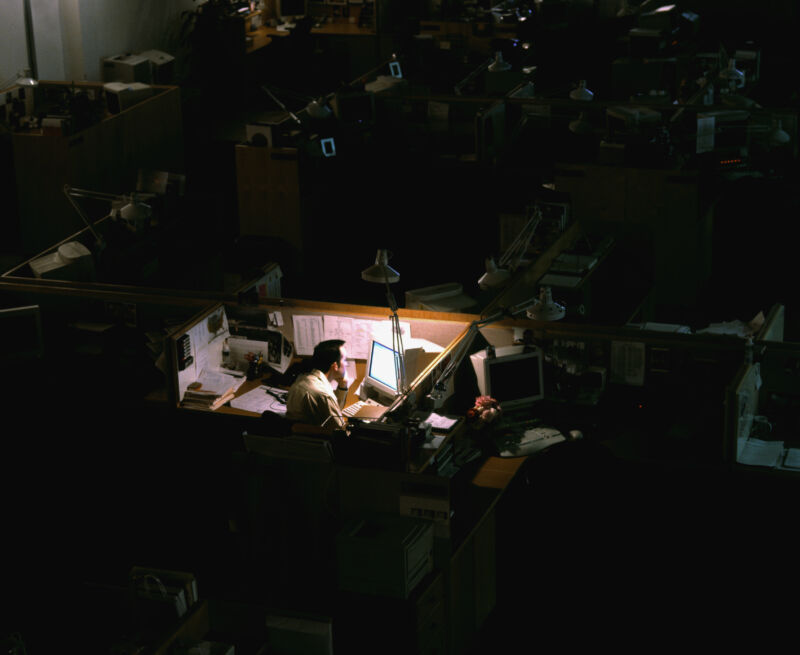 Man works late in dimly lit cubicle amid a dark office space