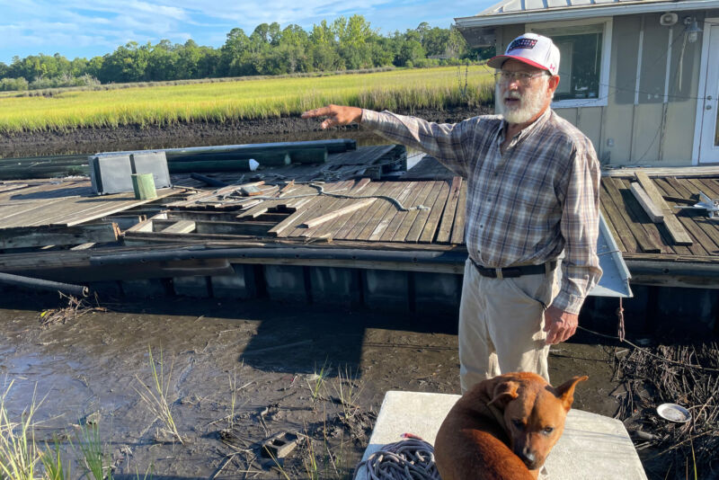 Older man points to the rising tide while standing on a dock.