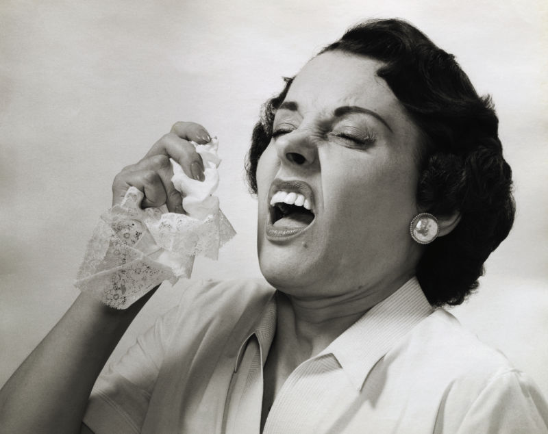 Picture shows a woman about to sneeze holding a handkerchief in her hand.