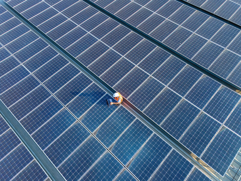 A single construction person set in the midst of a sea of solar panels.