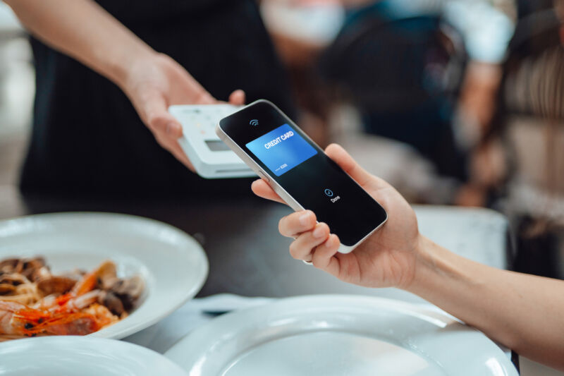 A raised iPhone-ish phone taps against a mobile payments square above restaurant dishes, including prawns.