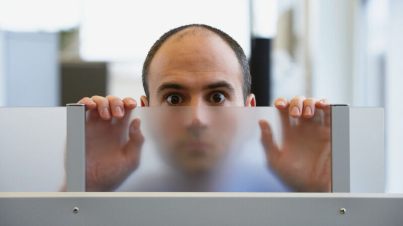 A man peers over a glass partition, seeking transparency.