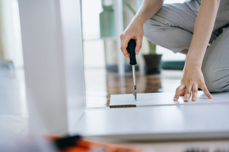 Cropped shot of young woman assembling furniture with a screwdriver. She is assembling a wooden cabinet in the living room in her new apartment