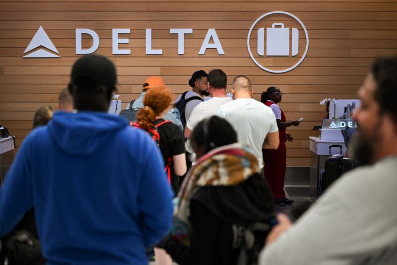 Delta Air Lines customers looking for missing bags wait in line in an airport baggage claim area.