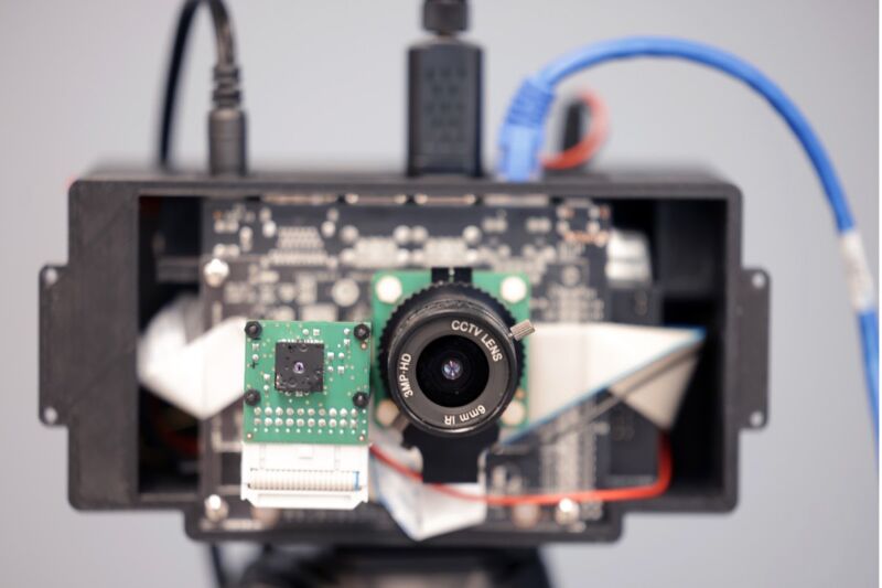 The front cover of a camera has been removed, revealing its internal components. A series of black and blue cords feed into the camera's connections.