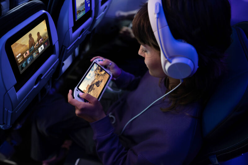 A child plays with a handheld games console while sitting in an airplane seat