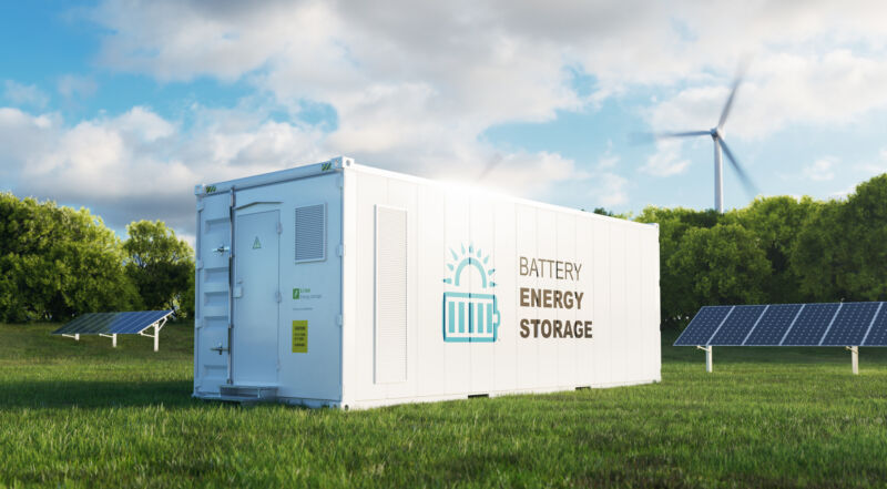 A shipping container labeled with a battery symbol, set among wind turbines and solar panels.