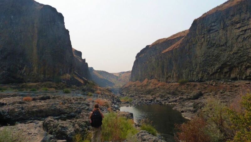 Image of a person in a stream-filled gap between two tall rock faces.