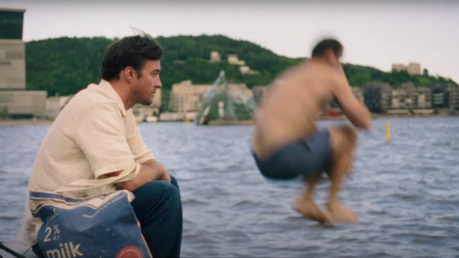 A man sits and watches another man jump into the water in Oslo.