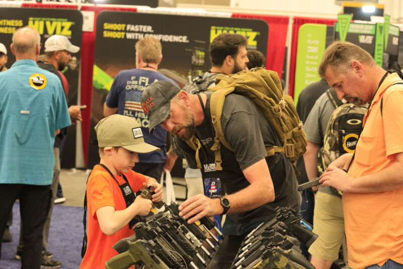 A man helps a boy look at a handgun during the National Rifle Association's Annual Meetings & Exhibits at the Indiana Convention Center in Indianapolis on April 16, 2023.