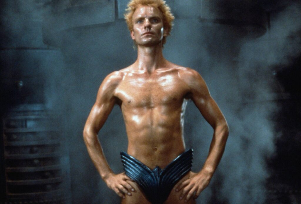 skinny man with spiky blonde hair naked except for a futuristic codpiece