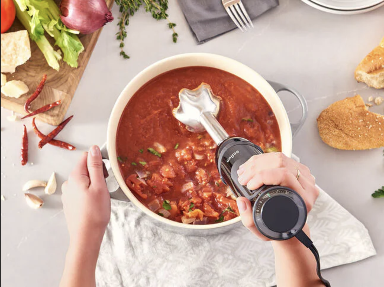 Overhead shot of hands holding a hand blender and stirring a bowl of a tomato-y broth.