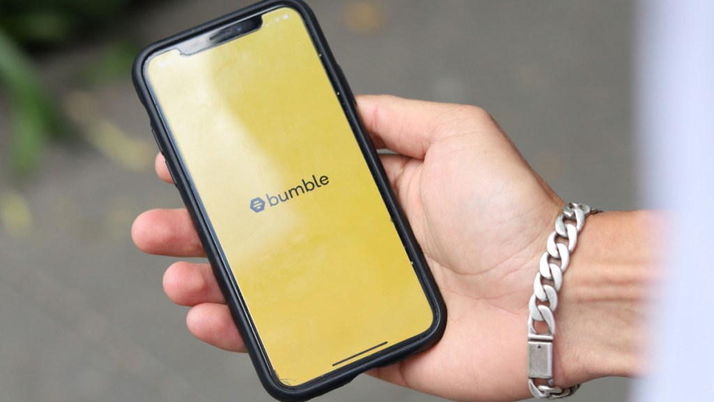 A person holding a cell phone in their hand. Bumble logo on phone.