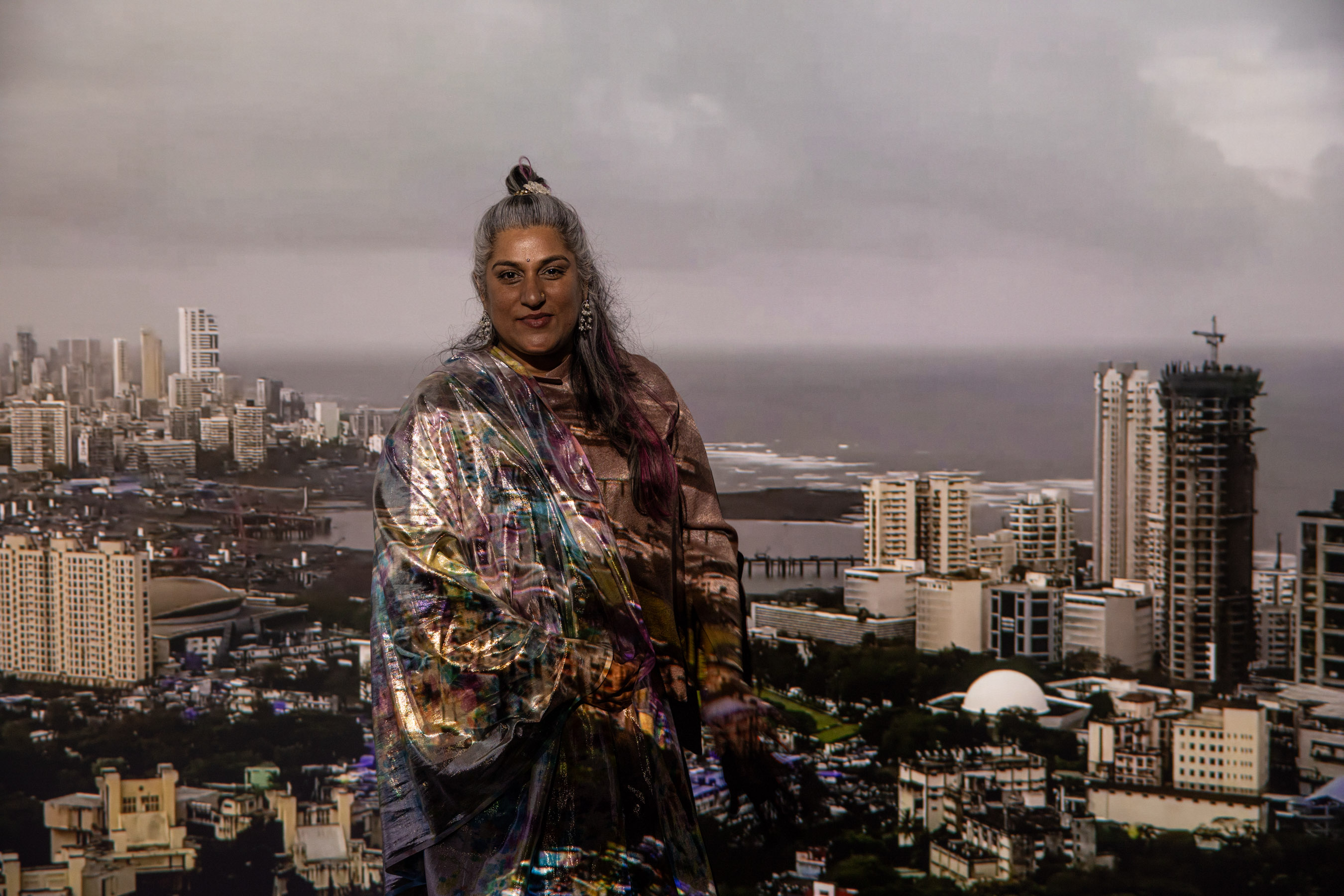 Shaina Anand stands in front of the projection of Bombay Tilts Down displayed in the final room of the exhibit, Video After Video: The Critical Media of CAMP.